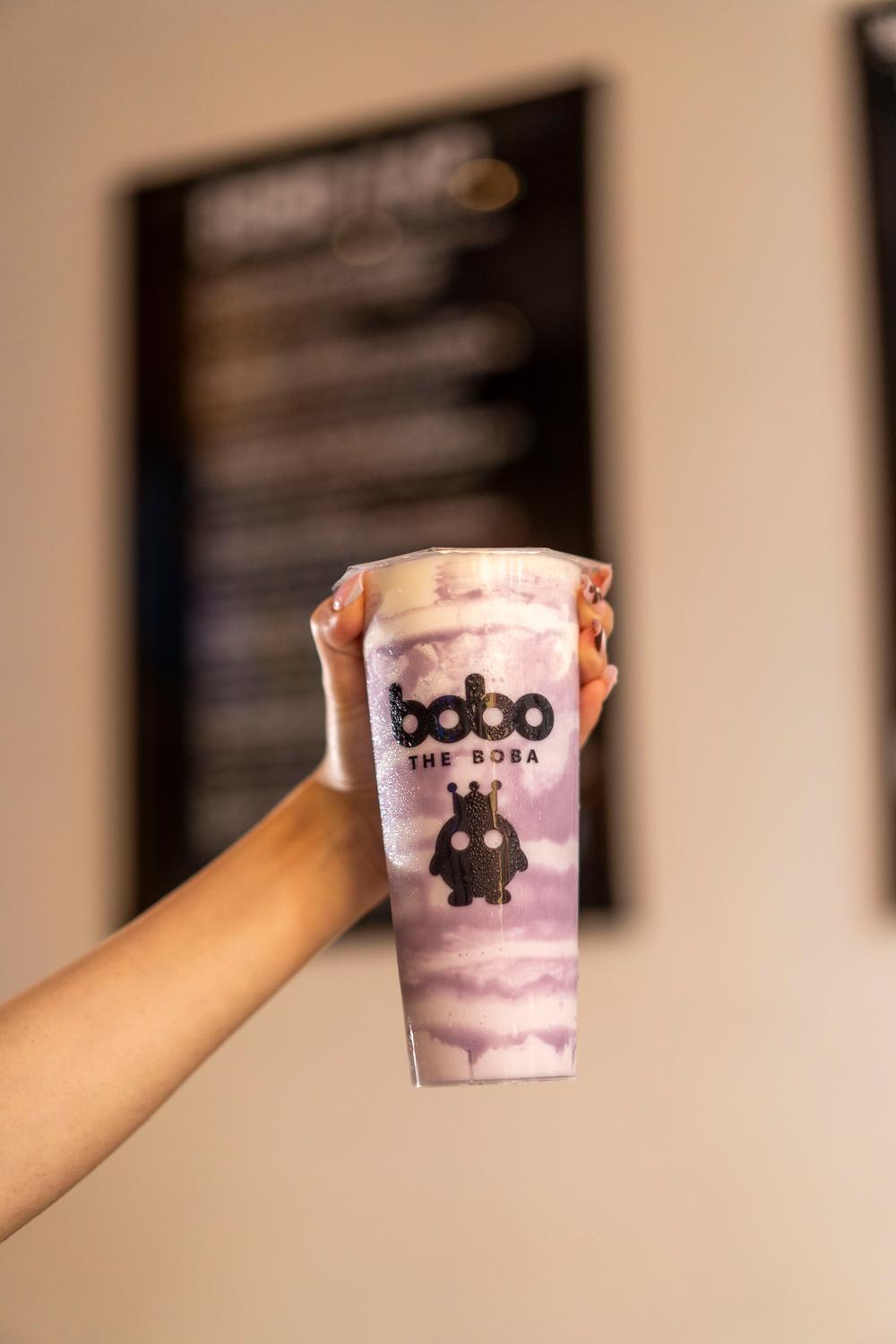 Hand holding a taro swirl milk tea in the shop